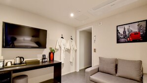 Ein modernes Hotelzimmer mit Flachbildfernseher, Schreibtisch mit Kaffeemaschine, Sofa und einem Bild eines roten Autos an der Wand.