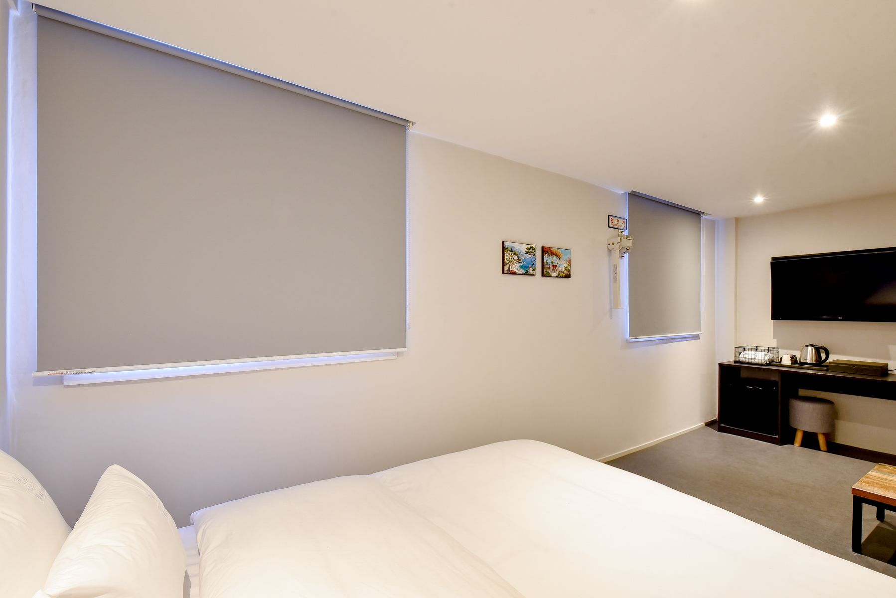 A hotel room with a bed, a desk, a television, and two paintings on the wall.