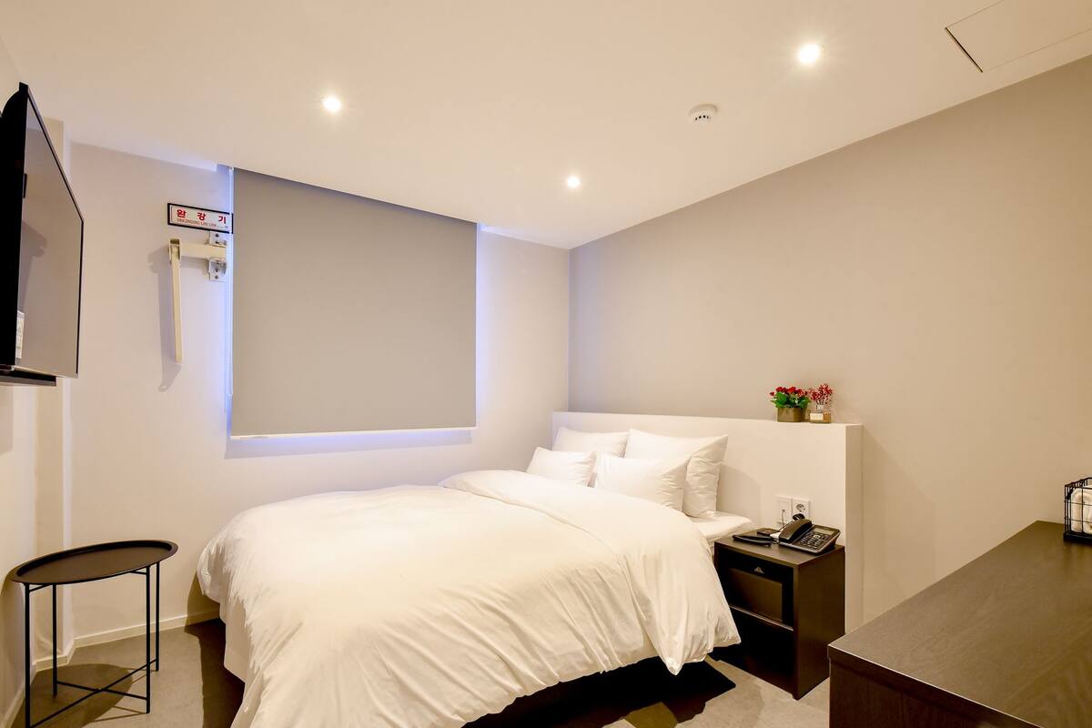 Ein modernes Hotelzimmer mit einem großen Bett, Nachttischen, einem Schreibtisch und einem an der Wand befestigten Fernseher.
