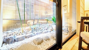 A room with a glass partition, wooden flooring, a chair, and a small indoor garden with rocks and plants.
