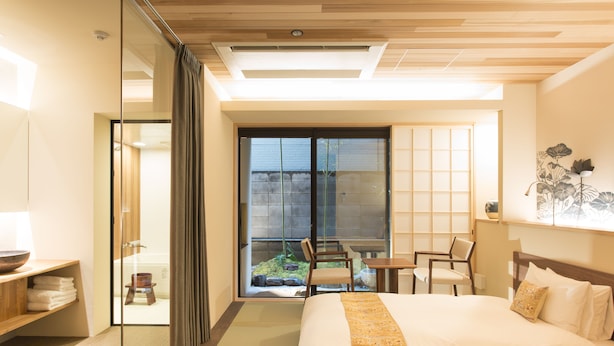 A hotel room with a large bed, a desk, a chair, and a view of a garden through a sliding door.