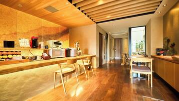 Eine moderne Küche mit Holzarbeitsplatten, einer Kaffeemaschine und einer Mikrowelle. Zwei Barhocker und ein Tisch mit Stühlen sind vorhanden. Der Boden ist aus Holz, und die Decke besteht aus Holzleisten.