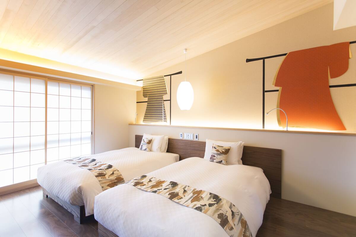 A hotel room with two beds, a large window with a view, and a modern light fixture.