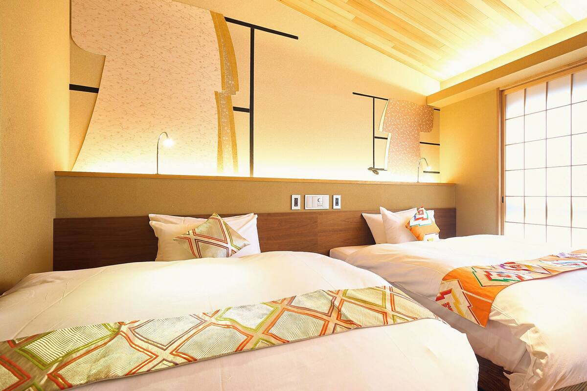 A hotel room with two beds, a wooden headboard, a large window with a view, and a wall-mounted light fixture.