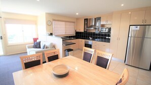 A modern kitchen with a dining area, featuring a large refrigerator, microwave, oven, and a dining table with chairs.
