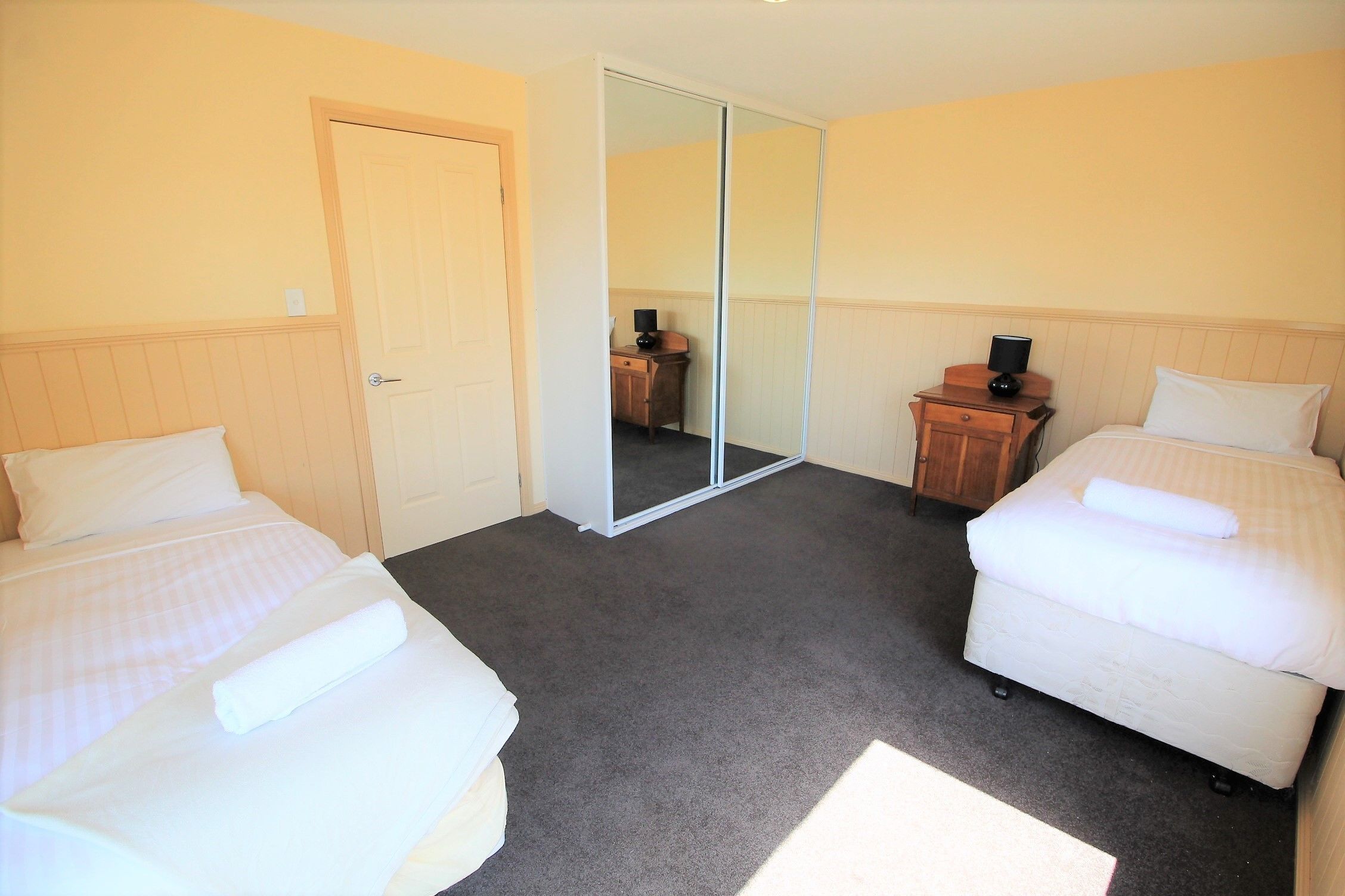 A room with two beds, a mirror, a wooden dresser, and a door.
