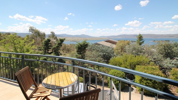 A balcony with a wooden table and chairs, overlooking a scenic landscape with trees and a body of water.