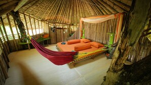 Een bamboehut met een bed, een hangmat en een tafeltje.