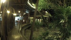 Een houten terras met een boogvormig pad dat leidt naar een gebouw met rieten dak.