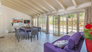 A spacious living area with a dining table, purple sofa, and large windows offering a view of the outdoors. - Gorgeous home in Krnica with sauna (Krnica)