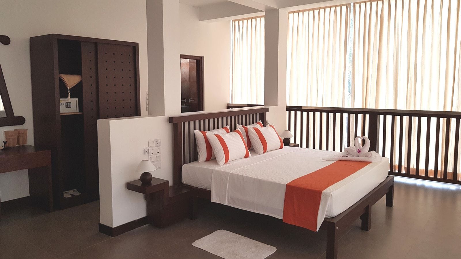Una habitación de hotel con cama, mesita de noche, lámpara, armario y una ventana con cortinas.