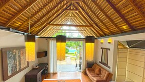 A spacious room with a high wooden ceiling, a sofa, a bed, and a dining area. - Blue Whale beach boutique Resort (Kandakuliya)