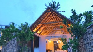 A modern building with a thatched roof, surrounded by lush greenery and palm trees. - Blue Whale beach boutique Resort (Kandakuliya)