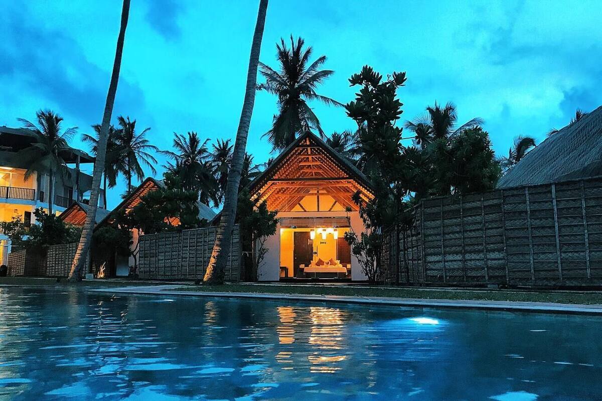 A resort with a swimming pool, palm trees, and a building with a thatched roof.