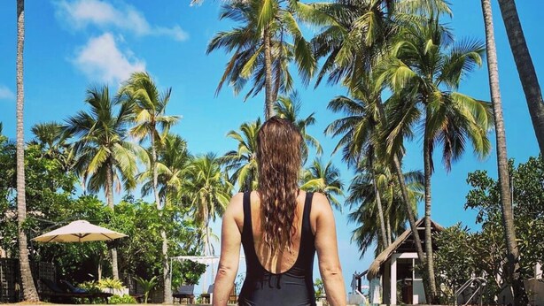 A woman in a black swimsuit sitting at the edge of a clear pool surrounded by palm trees. - Blue Whale beach boutique Resort (Kandakuliya)
