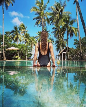 A woman in a black swimsuit sitting at the edge of a clear pool surrounded by palm trees. - Blue Whale beach boutique Resort (Kandakuliya)