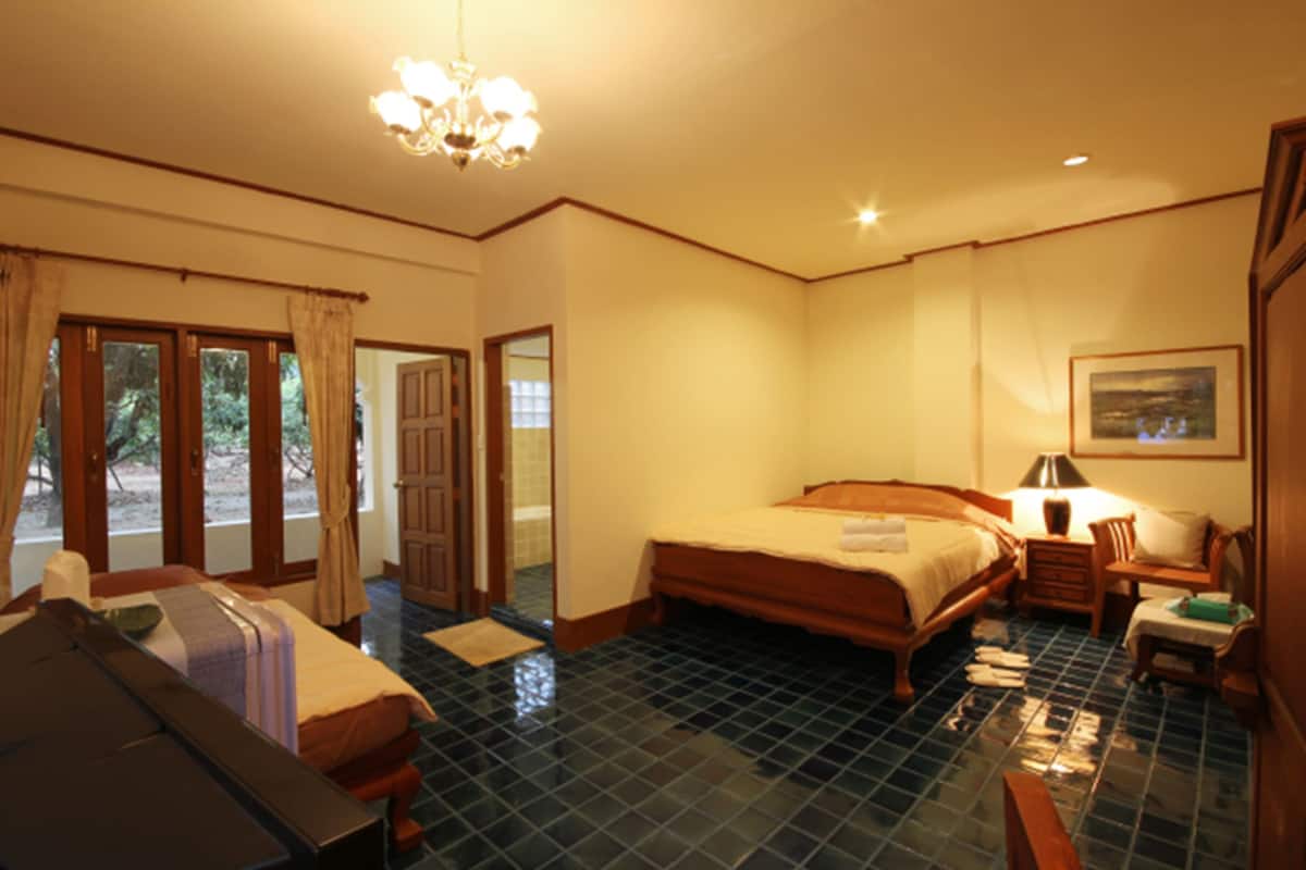 A hotel room with a large bed, a desk with a lamp, a chair, a small table, and a painting on the wall.