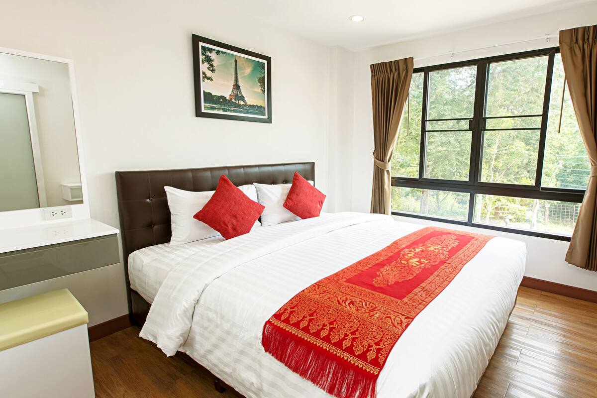 Quarto de hotel com cama grande, mesa de cabeceira, espelho, janela com cortinas e um quadro na parede.