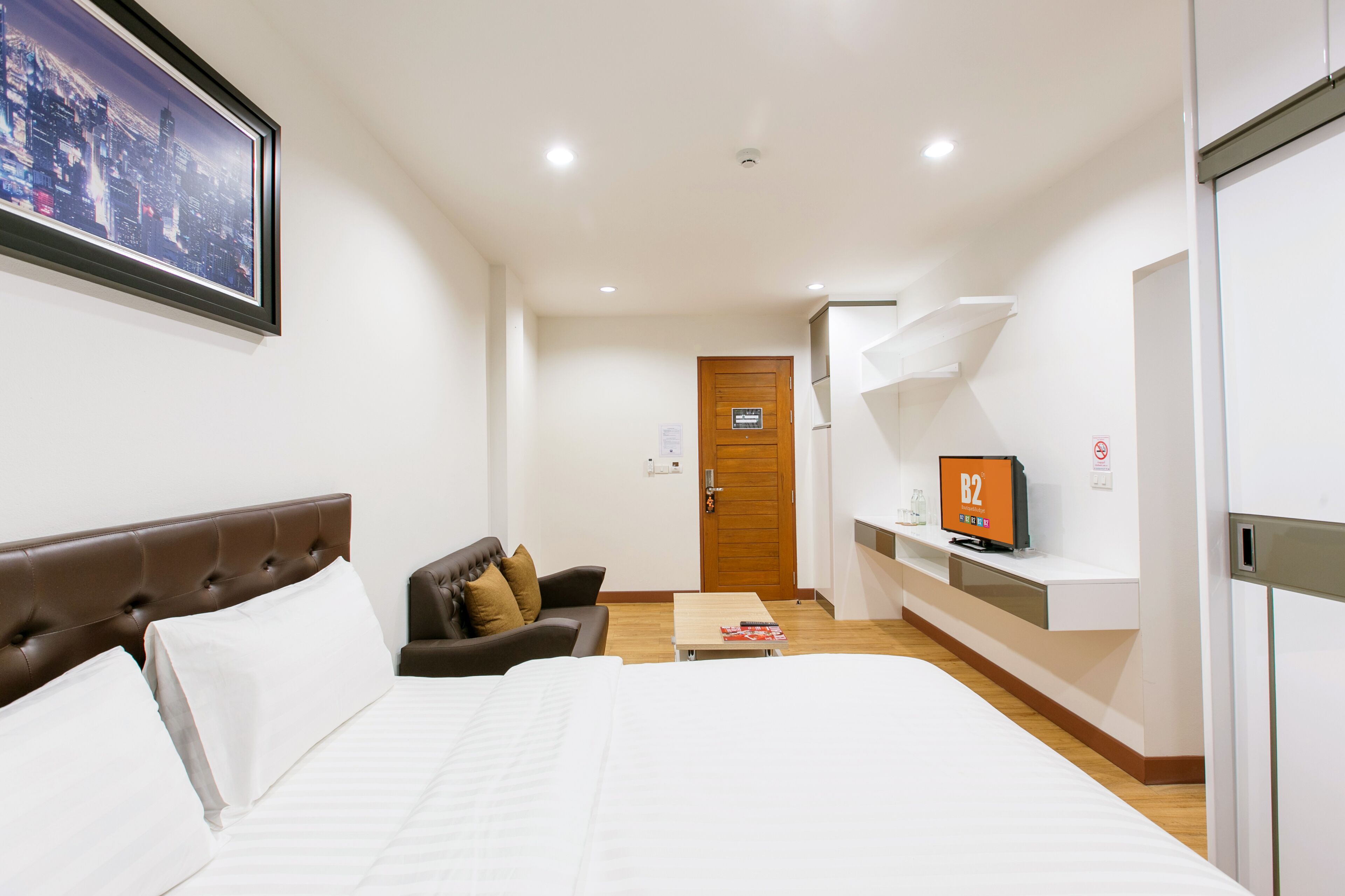 A hotel room with a large bed, a sofa, a TV, and a cityscape view.