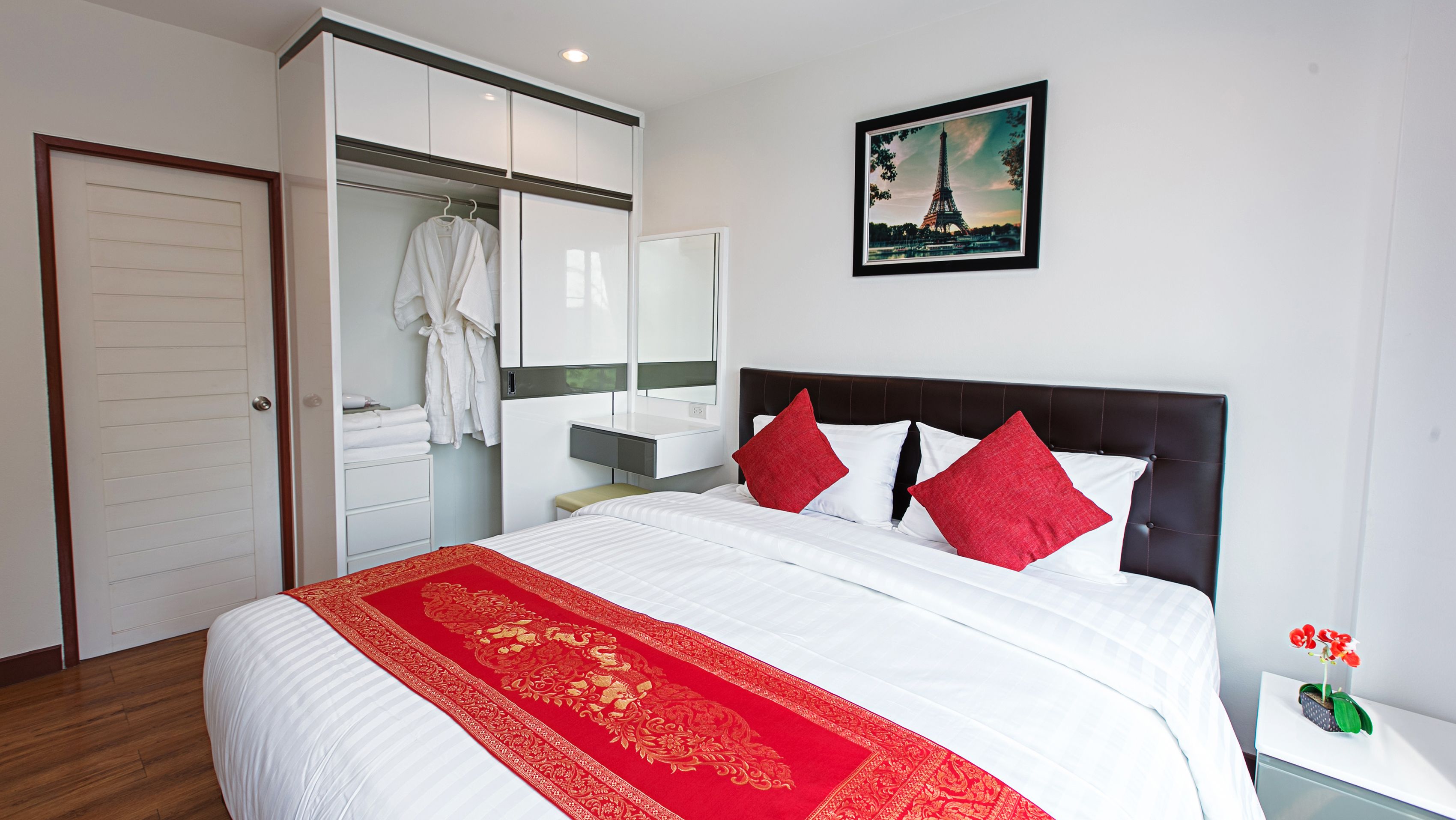 A hotel room with a large bed, a wardrobe, a bathroom, and a painting of the Eiffel Tower.