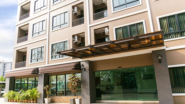 Un hotel de varios pisos con balcones, ventanas amplias y un acceso cubierto con plantas en macetas.