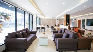 Amplia sala de estar con dos sofás, una mesa de centro y una mesa de comedor con sillas. Grandes ventanales ofrecen luz natural y vistas al exterior.