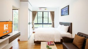 Habitación de hotel con cama, televisión, sofá, ventana con cortinas y un cuadro en la pared.