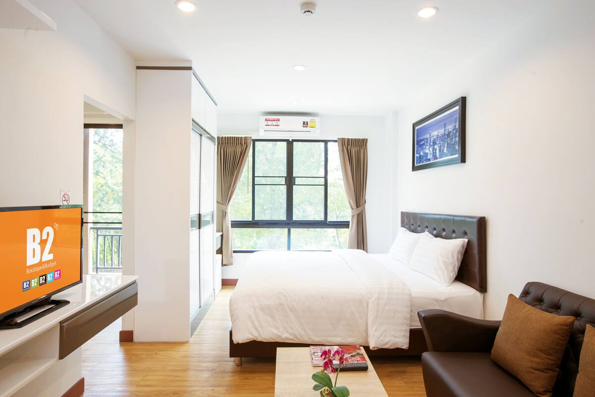 Quarto de hotel com cama, televisão, sofá, janela com cortinas e um quadro na parede.