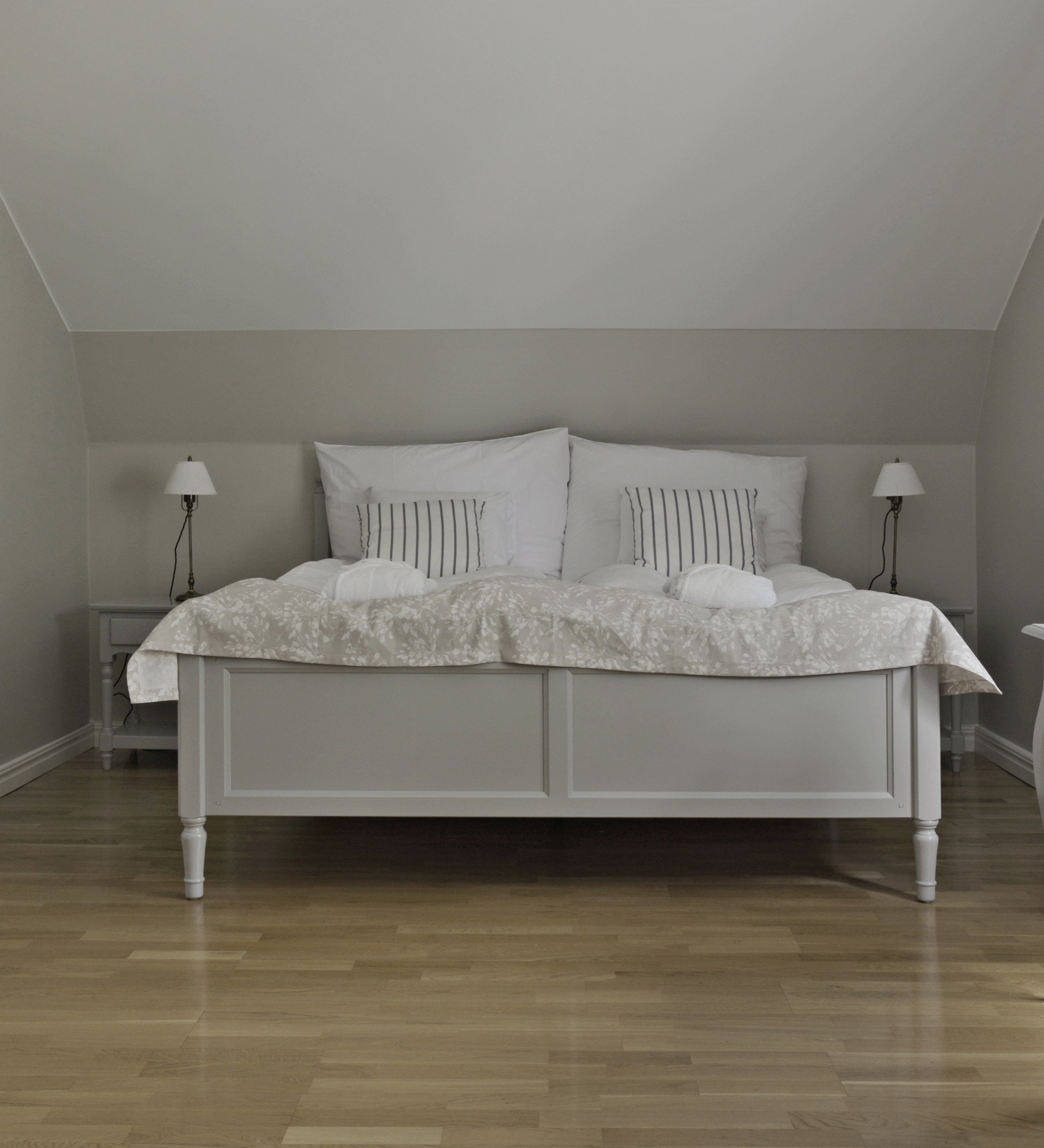 Una camera da letto con un letto bianco, due comodini e un pavimento in legno.