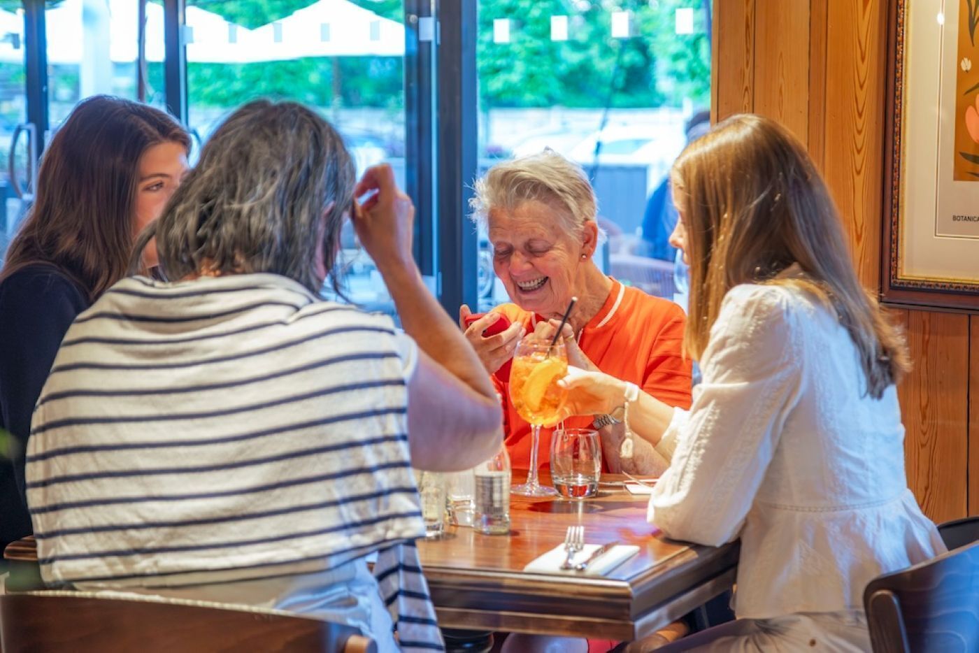 A group of people seated at a table in a restaurant with a view of the outdoors.