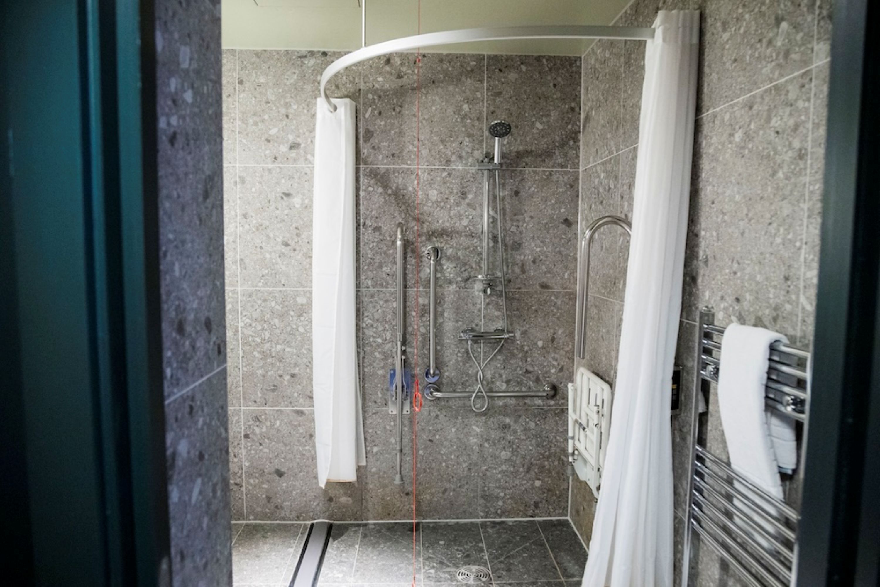 Zona de ducha con mampara curva, ducha de mano y grifo empotrado en la pared.