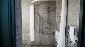 Zona de ducha con mampara curva, ducha de mano y grifo empotrado en la pared.