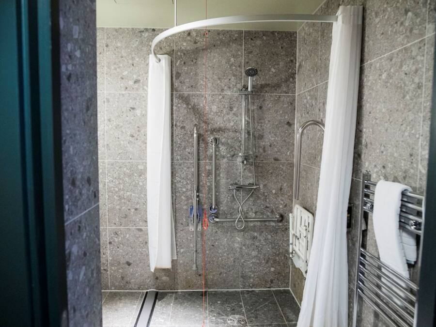 Zona de ducha con mampara curva, ducha de mano y grifo empotrado en la pared.
