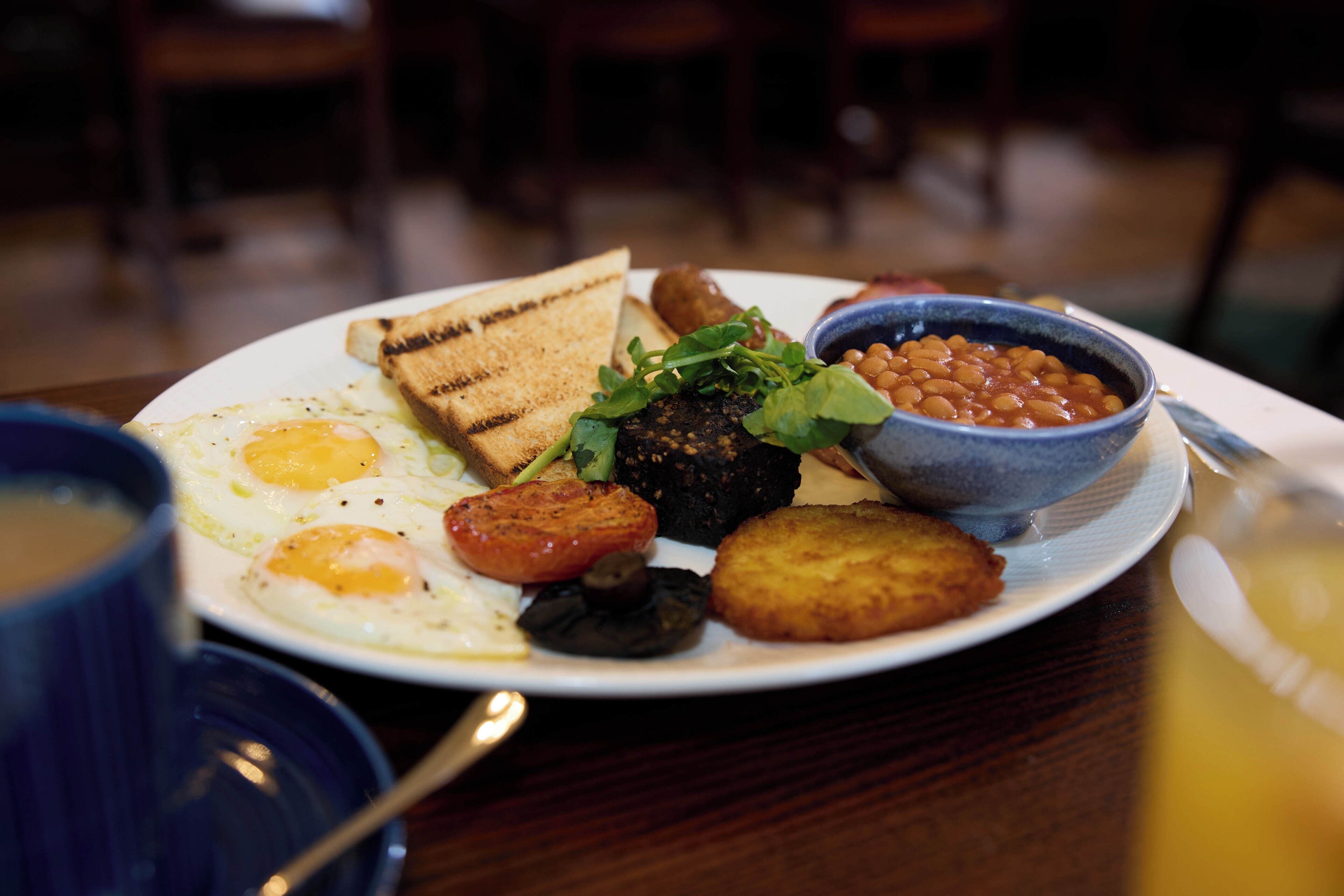 A plate of breakfast food including eggs, toast, beans, and a fried item.