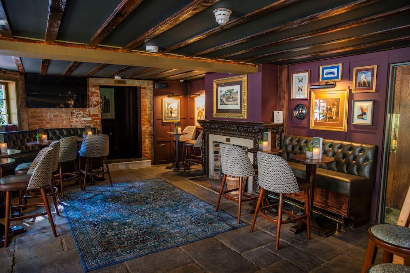 Un espace bar agrémenté de poutres en bois, d’une cheminée, de tabourets de bar et de tableaux encadrés aux murs.