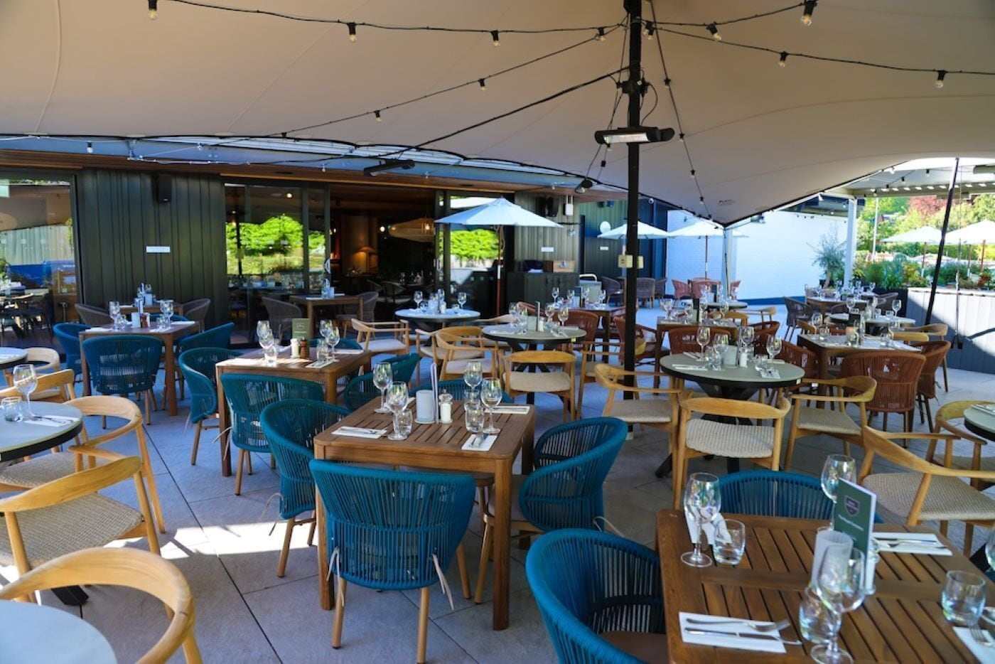 Un espacio exterior para comer con mesas, sillas, sombrillas y vistas al interior del restaurante.
