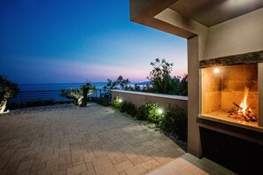 A paved outdoor patio with a fire feature and a view of the ocean at dusk.