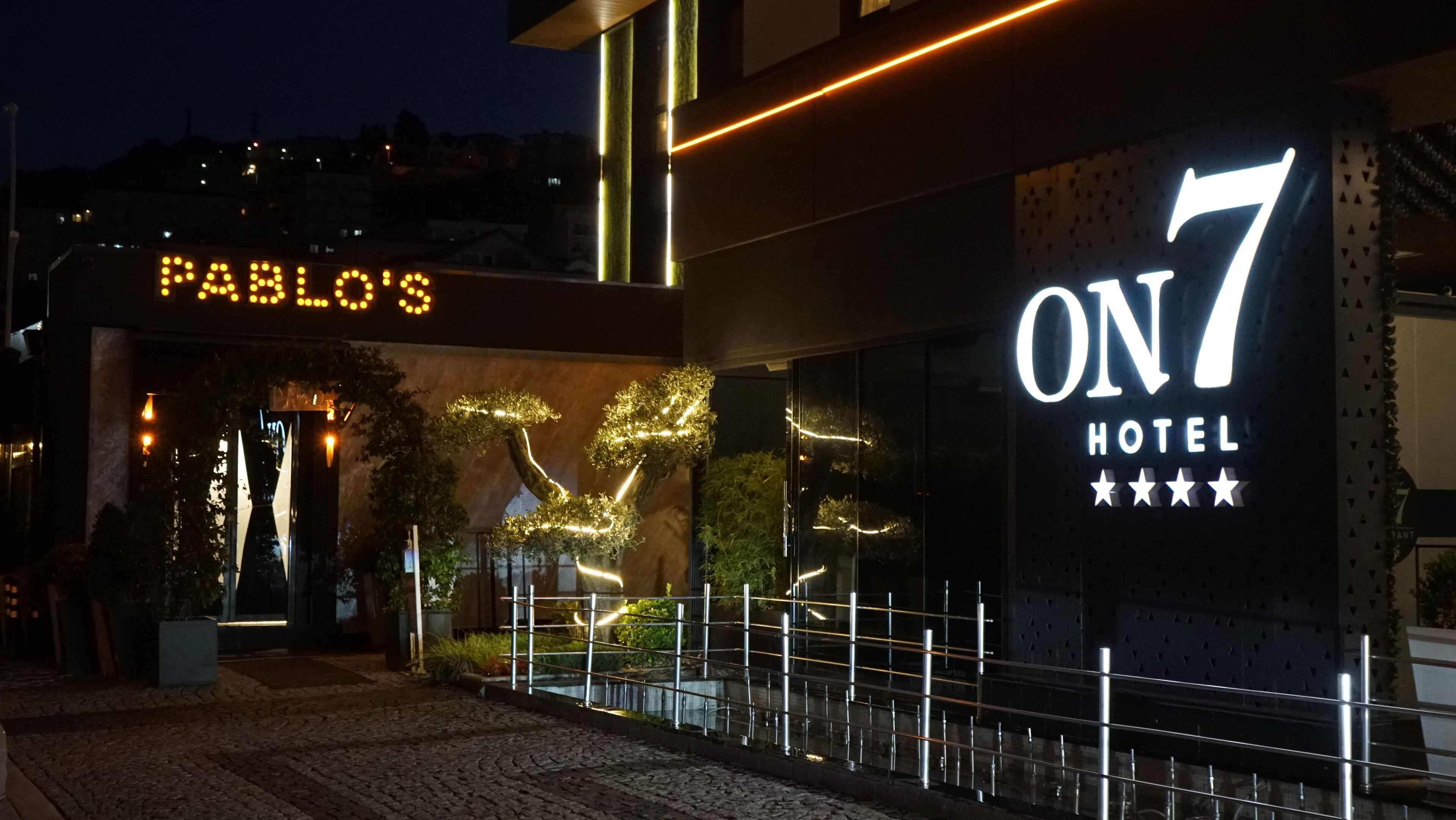 L’entrée d’un hôtel, avec une enseigne indiquant « ON 7 HOTEL » et une plus petite enseigne au-dessus, sur laquelle on peut lire « PABLO’S ».