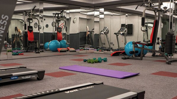 Un gimnasio con equipo de ejercicio, espejos y suelo cubierto de alfombra.