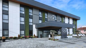 A modern hotel with a prominent 'ON7' sign, a paved entrance, and a landscaped garden area.