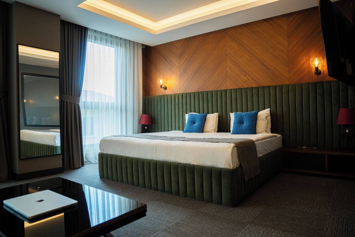 A modern hotel room with a large bed, a desk, and a mirror.