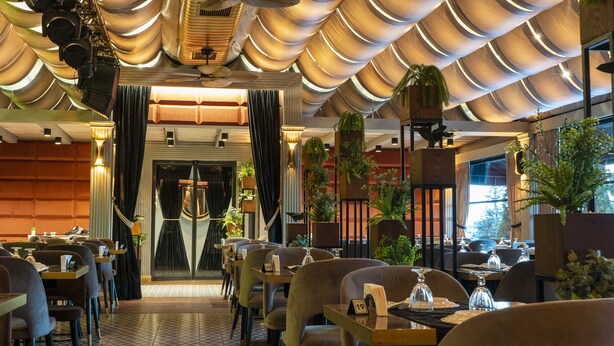 A restaurant with a modern interior, featuring a patterned ceiling, dark curtains, and multiple tables with chairs.