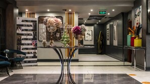 A modern lobby with a central round table displaying floral arrangements, a vertical photo display, and a reception desk.