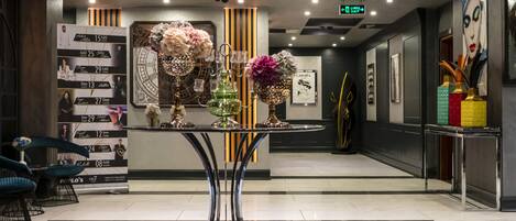 Un vestíbulo moderno con una mesa redonda central que exhibe arreglos florales, un panel vertical de fotografías y un mostrador de recepción.