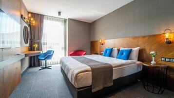 Una habitación de hotel moderna con una cama grande, un escritorio, una silla roja y una pequeña mesa con un jarrón de flores.