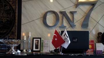 A reception desk with a glass bowl, candles, a framed photo, and flags. The wall behind has the number 'ON7' and a globe.
