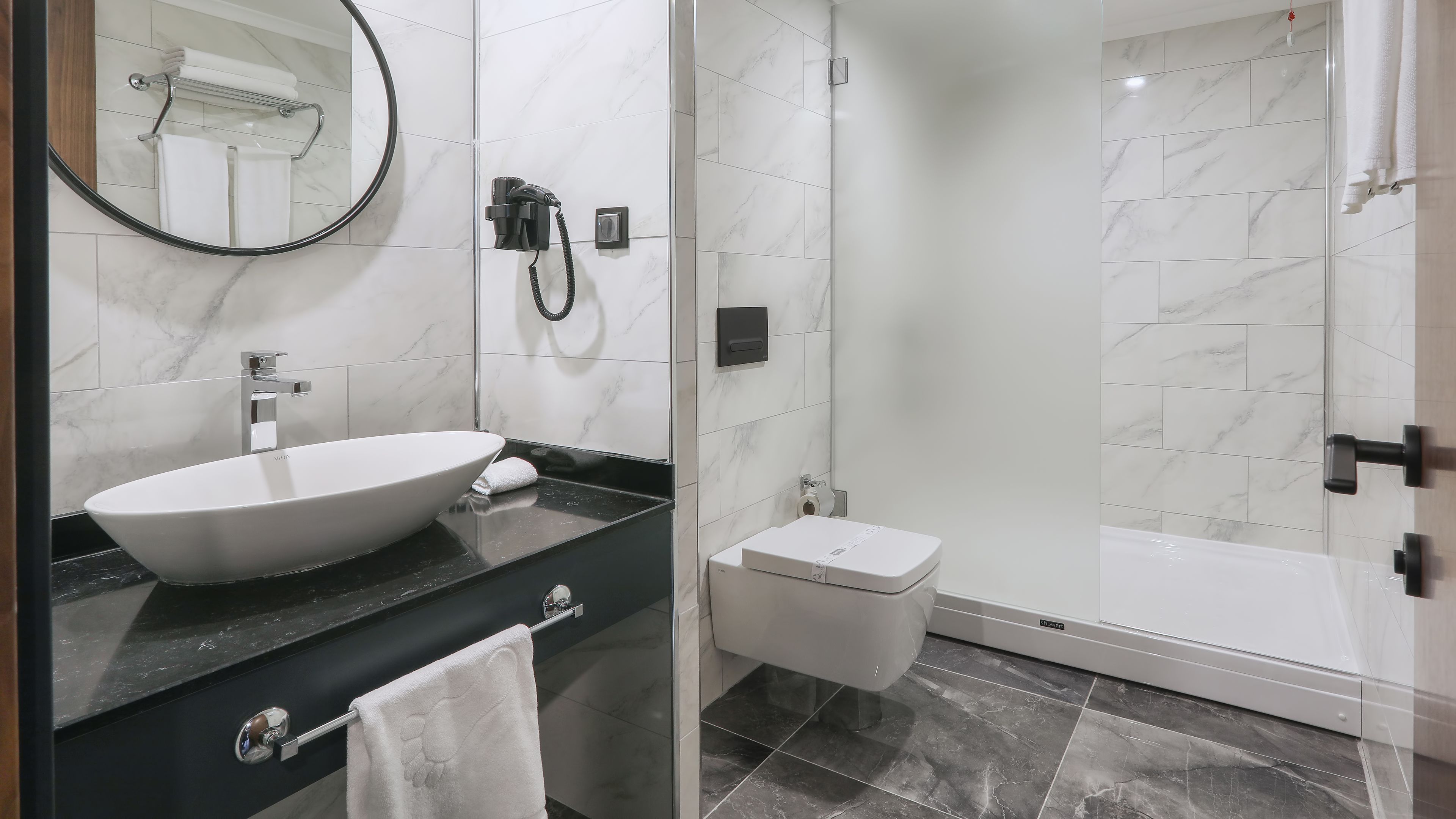 Un baño con un lavamanos grande de color blanco, un inodoro y una ducha con cerramiento de vidrio.