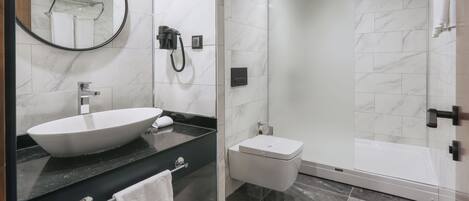 Un baño con un lavamanos grande de color blanco, un inodoro y una ducha con cerramiento de vidrio.