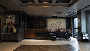 A modern hotel lobby with a reception desk, seating area, and large windows.
