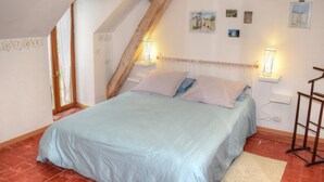 Une chambre avec un plafond en pente, un lit recouvert d’une courtepointe bleu clair, deux lampes fixées au mur et une échelle en bois.